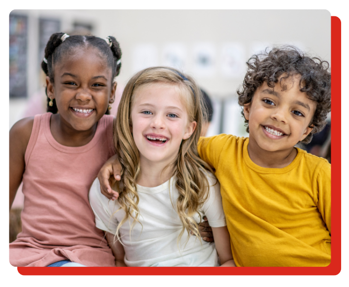3 kids sitting in classroom looking at the camera. Red keyline outline