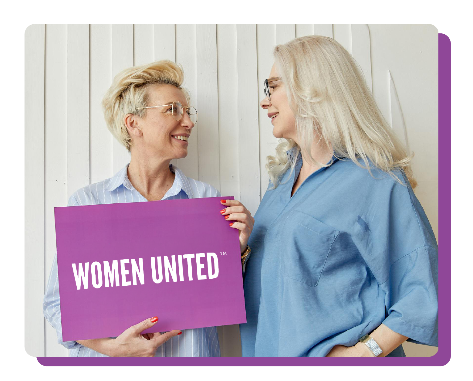 Women United, become a member. Two women looking at each other holding a Women United sign